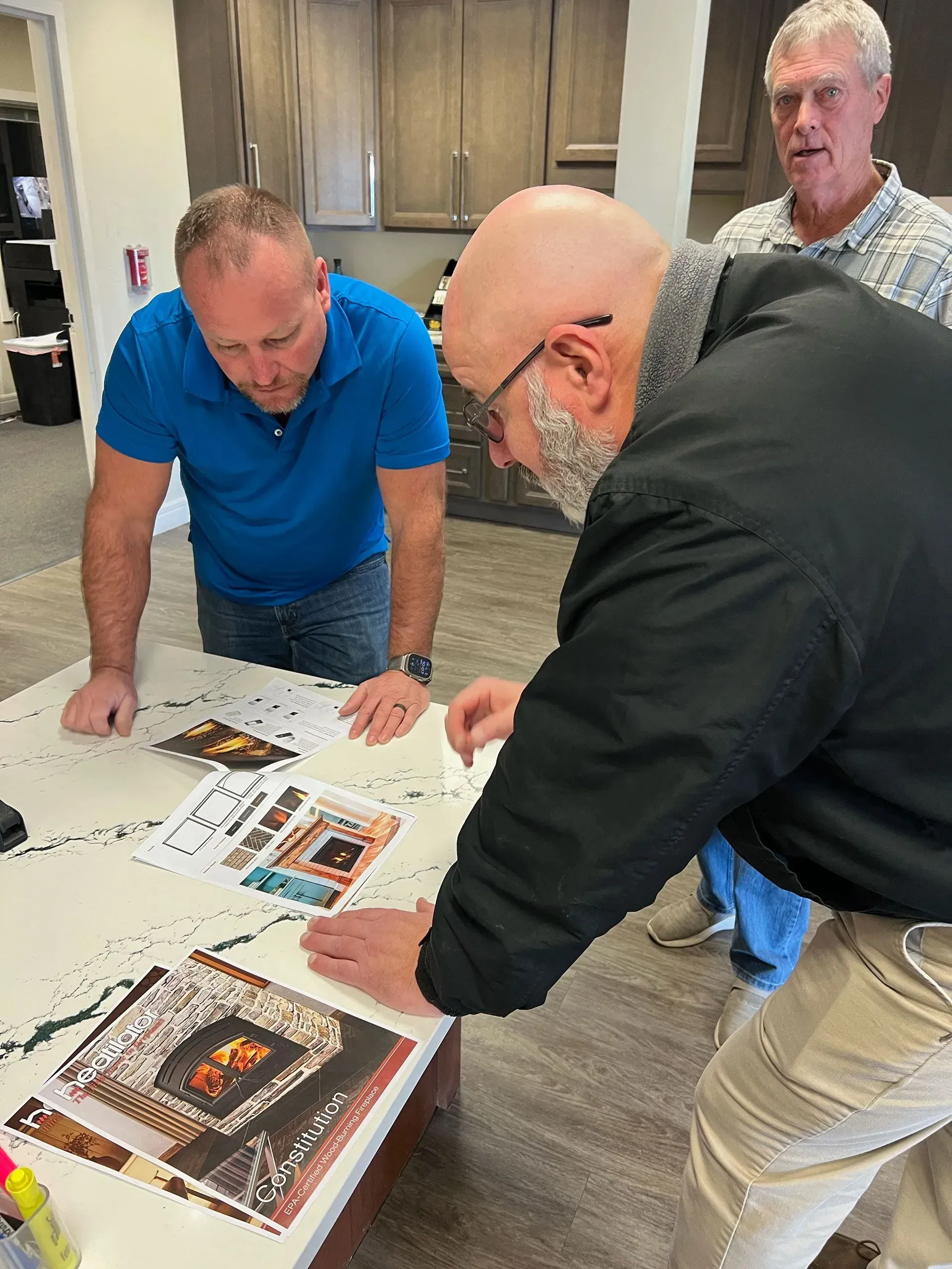 Three men leaning over a table reviewing printed materials in a room