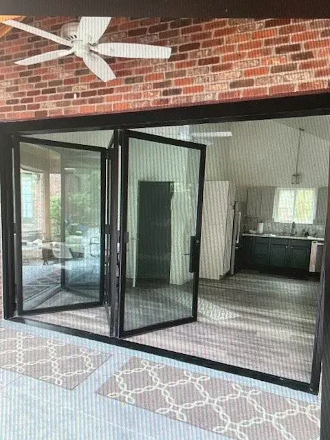 Outdoor patio with black folding glass doors opening to a screened porch and brick wall ceiling fan