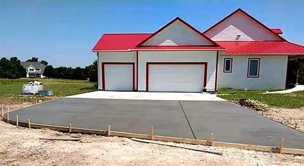 New house with red roof and large concrete driveway under construction