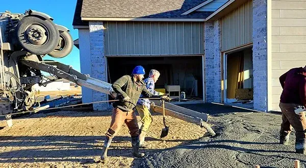 Construction workers guiding a concrete pump hose beside a house under construction