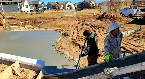 Workers pouring concrete at a new house foundation on a sunny construction site.