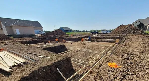 Construction site with excavated trench, dirt piles, and workers under a clear blue sky