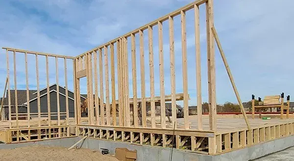 Wood-framed house under construction on a concrete foundation under a blue sky