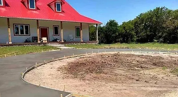 House with red roof beside a curved driveway and bare yard under a clear blue sky