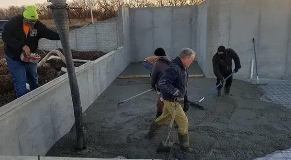 Workers leveling wet concrete in a large foundation area outdoors