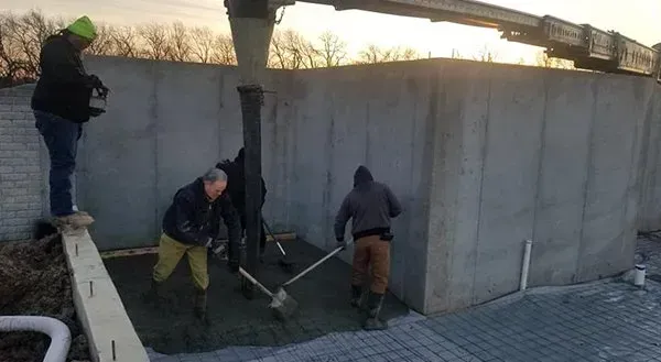 Workers repairing a concrete wall beside a bridge at dusk
