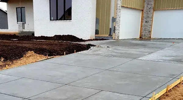 Concrete walkway beside a newly built house with dark mulch and unfinished landscaping