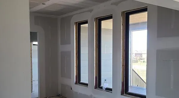 Empty room with white walls and three tall windows letting in daylight.