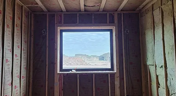 Unfinished wooden room with insulation and a small window showing a bright desert view.