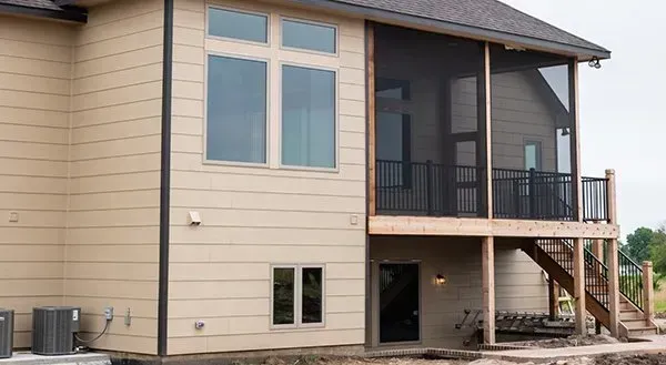 Exterior of a beige house with a covered porch, balcony, and stairs on the side