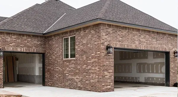 Brick house exterior with open garage and driveway under gray shingled roof