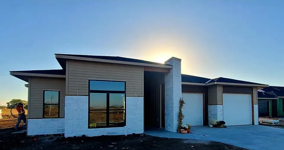 Modern single-story house exterior with large windows, white and gray facade, and driveway at sunset