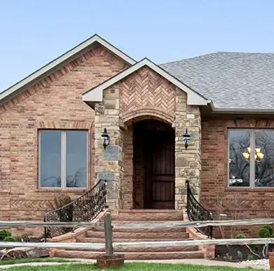 Brick house front with stone entry, arched doorway, and a wooden fence in front