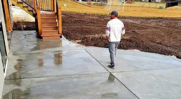 Person walking on a wet concrete sidewalk beside wooden stairs at a construction site