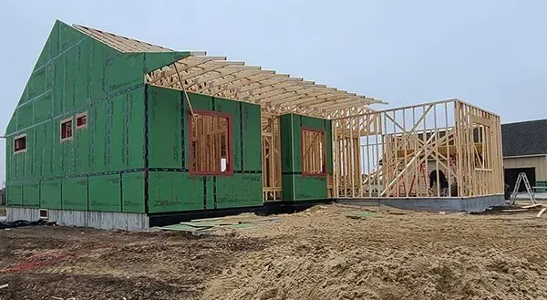 Partially built house with green sheathing and wooden roof framing on a dirt lot