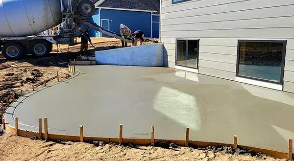 Freshly poured concrete slab beside a building, with a cement truck in the background.