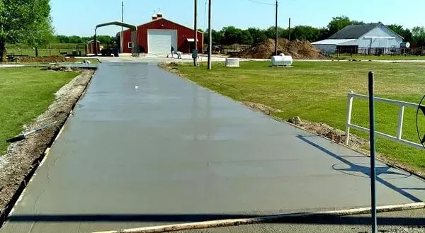 Concrete driveway leading to a red barn-like building on a rural property