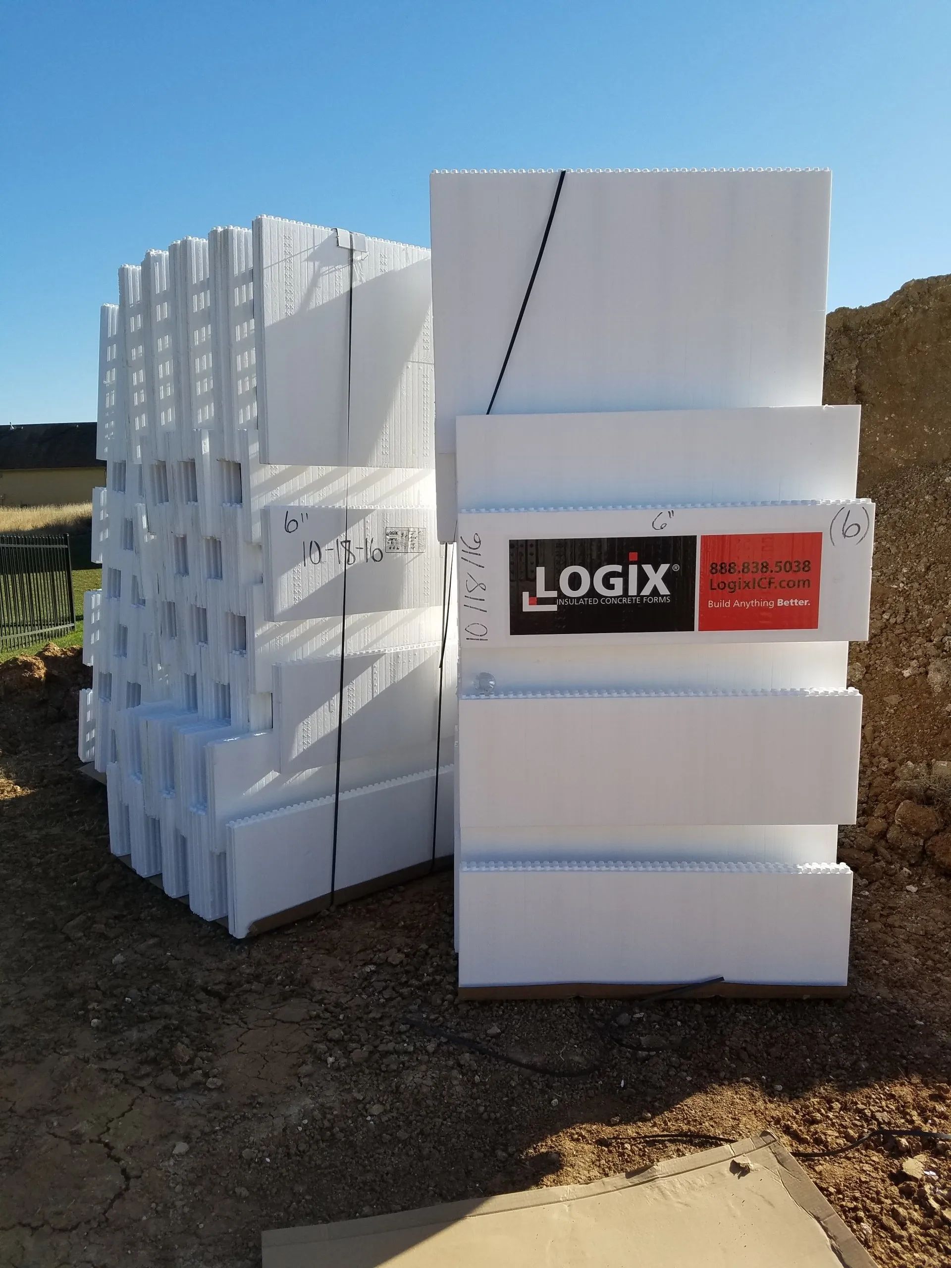 Stacked white foam insulation boards outdoors, one package labeled LOGIX.