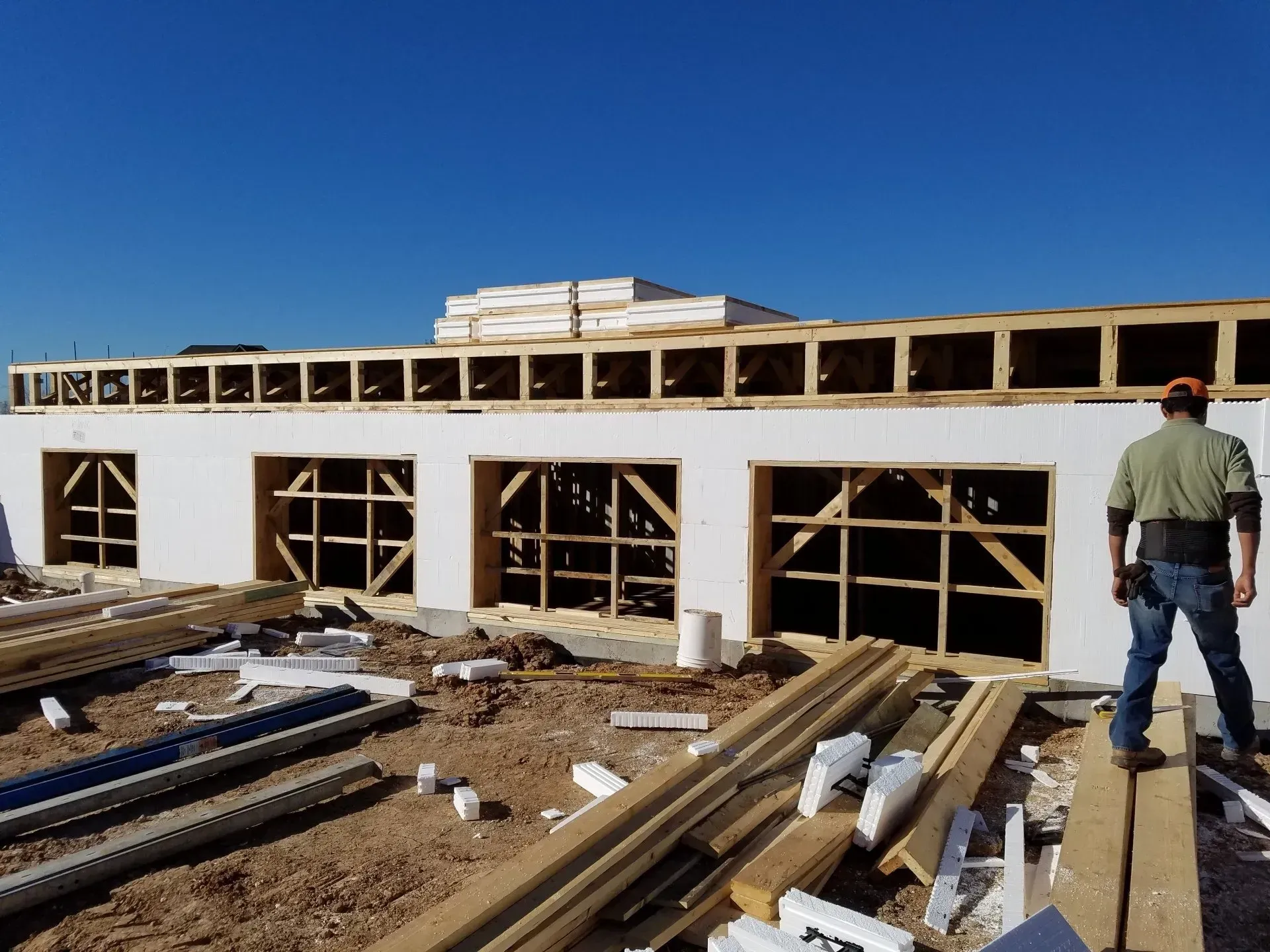 Partially built wooden structure under construction, with lumber in the foreground and a worker standing outside
