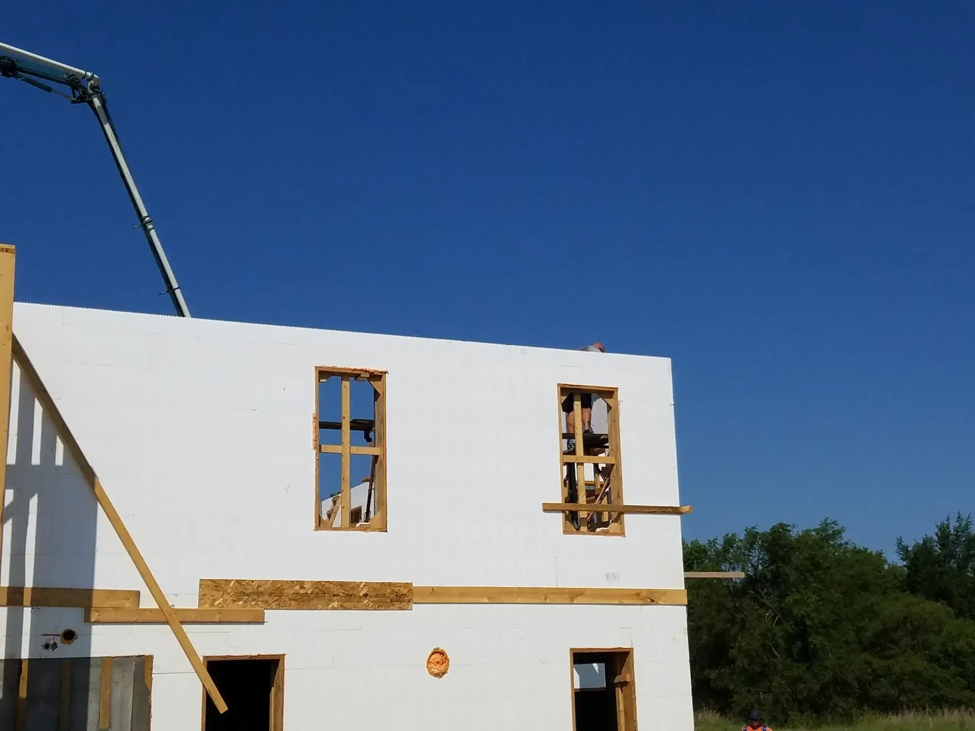 Partially built white house with wooden-framed windows against a clear blue sky.