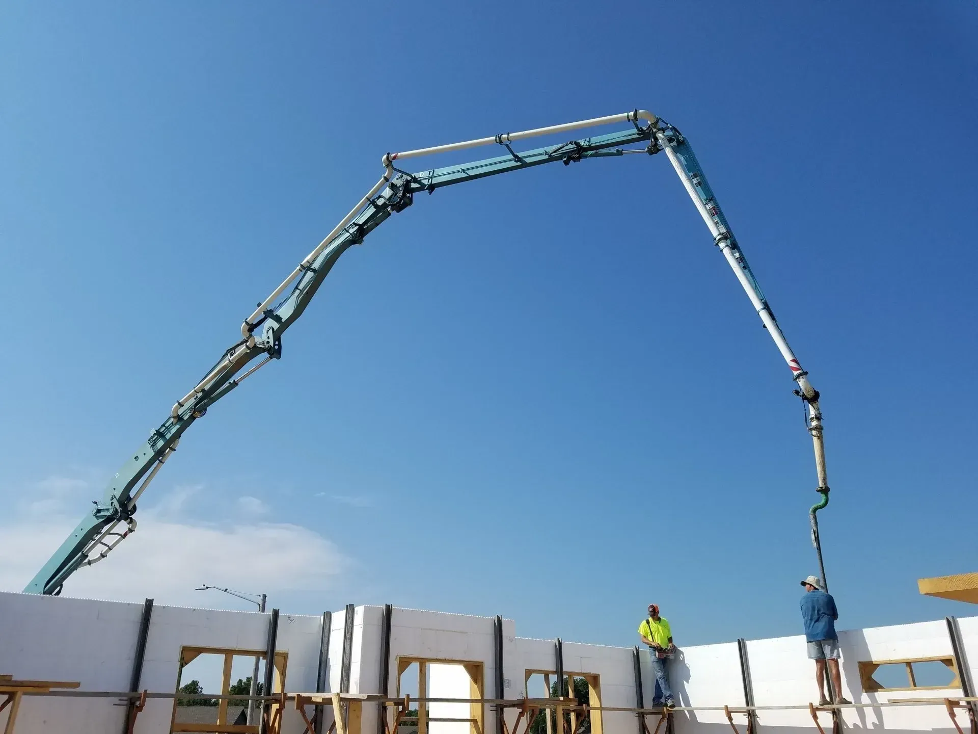Concrete pump truck arm pouring at a construction site under a clear blue sky