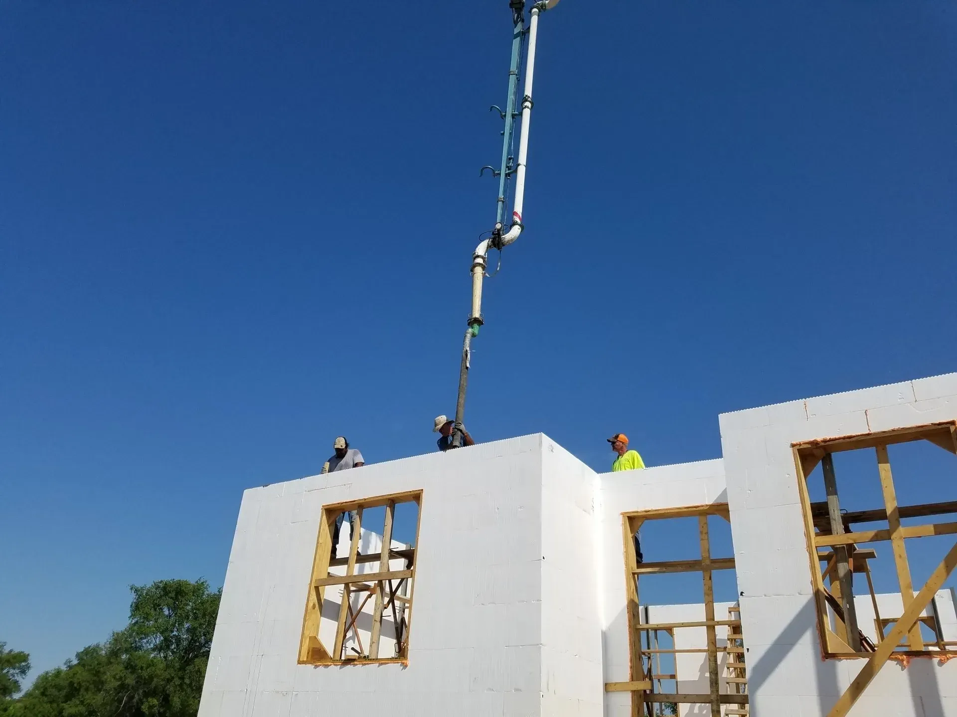 Workers pour concrete into a white building wall from a crane under a clear blue sky