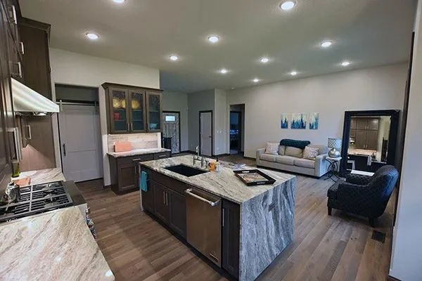 Open-concept kitchen and living room with island, gray couches, and hardwood floors.