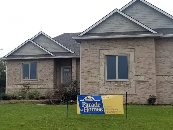 Single-story stone house with a Parade of Homes sign on the lawn