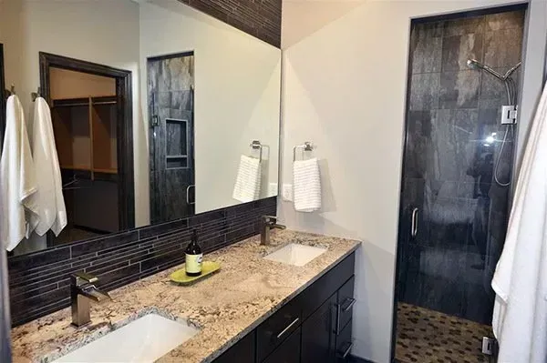 Modern bathroom vanity with granite countertop, large mirror, sink, and glass-enclosed shower