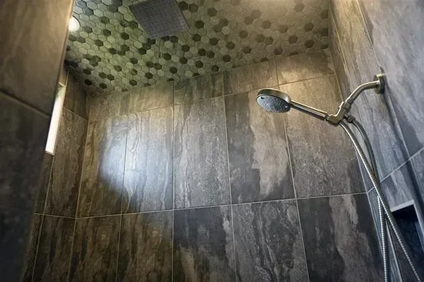 Modern tiled shower with dark walls, pebble ceiling accent, and a handheld showerhead