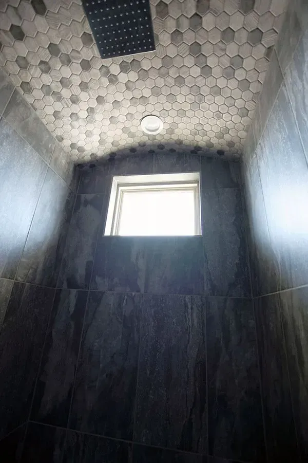 Small tiled bathroom shower with a window and ceiling light, viewed upward.