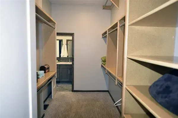 Walk-in closet with built-in shelving, hanging rods, and carpeted floor leading to a doorway.
