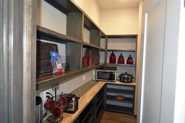 Built-in pantry with wooden shelves, microwave, kettle, and red glass jars in a narrow alcove