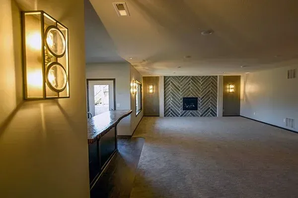 Empty carpeted living room with wall sconces, large windows, and a fireplace at the far end