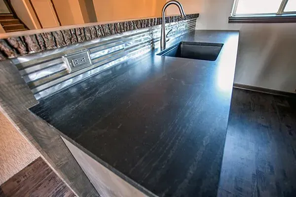 Modern kitchen with dark granite countertop, stainless sink, and stone tile backsplash