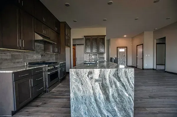 Modern kitchen with dark cabinets, granite island, stainless appliances, and gray wood-style flooring