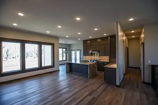 Open-concept modern kitchen and living area with dark wood floors, gray cabinets, and large windows