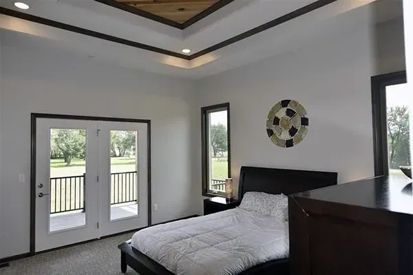 Bright modern bedroom with bed, double doors, windows, and a tray ceiling with recessed lights