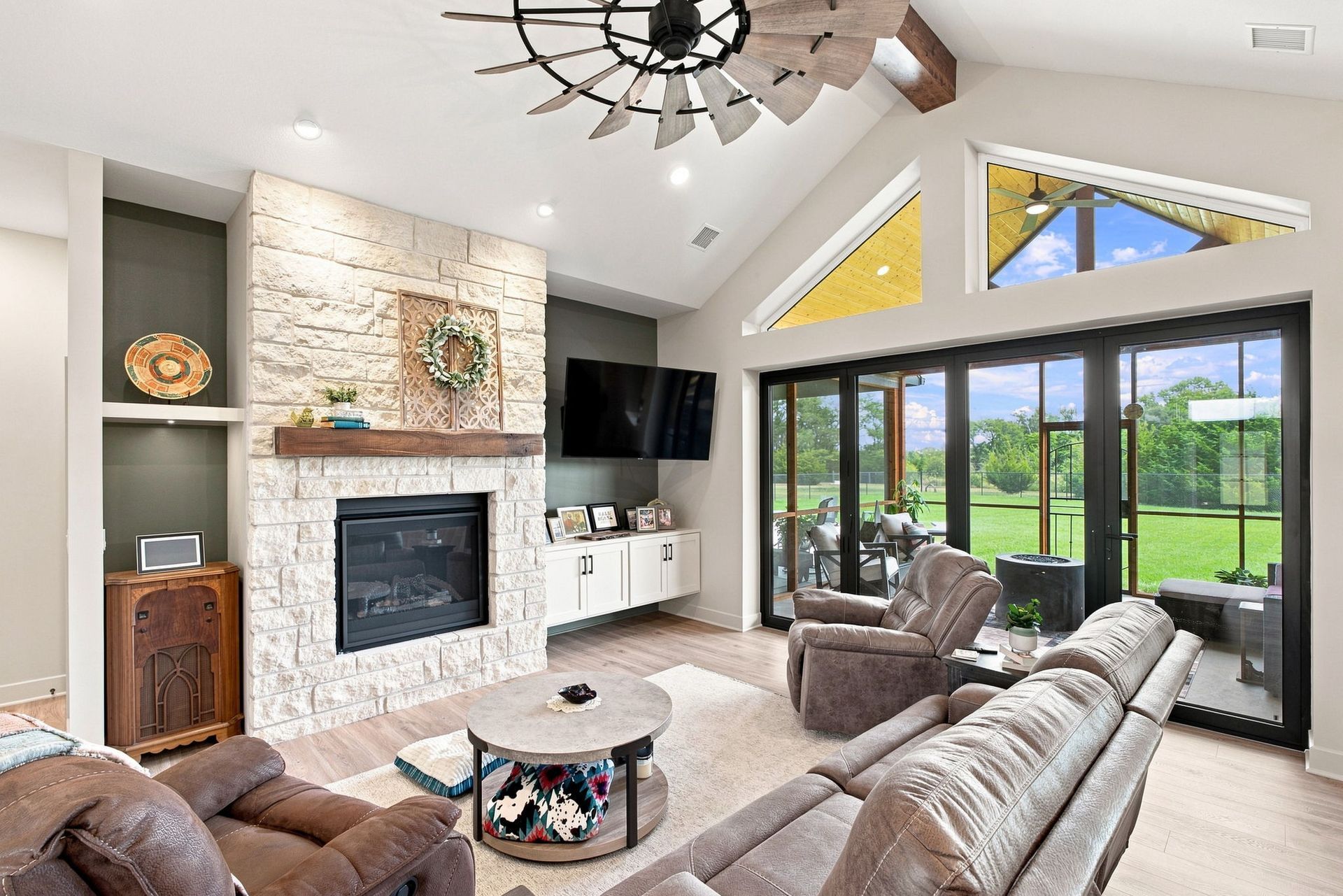 Bright living room with stone fireplace, sectional sofa, and large glass doors to a green backyard.