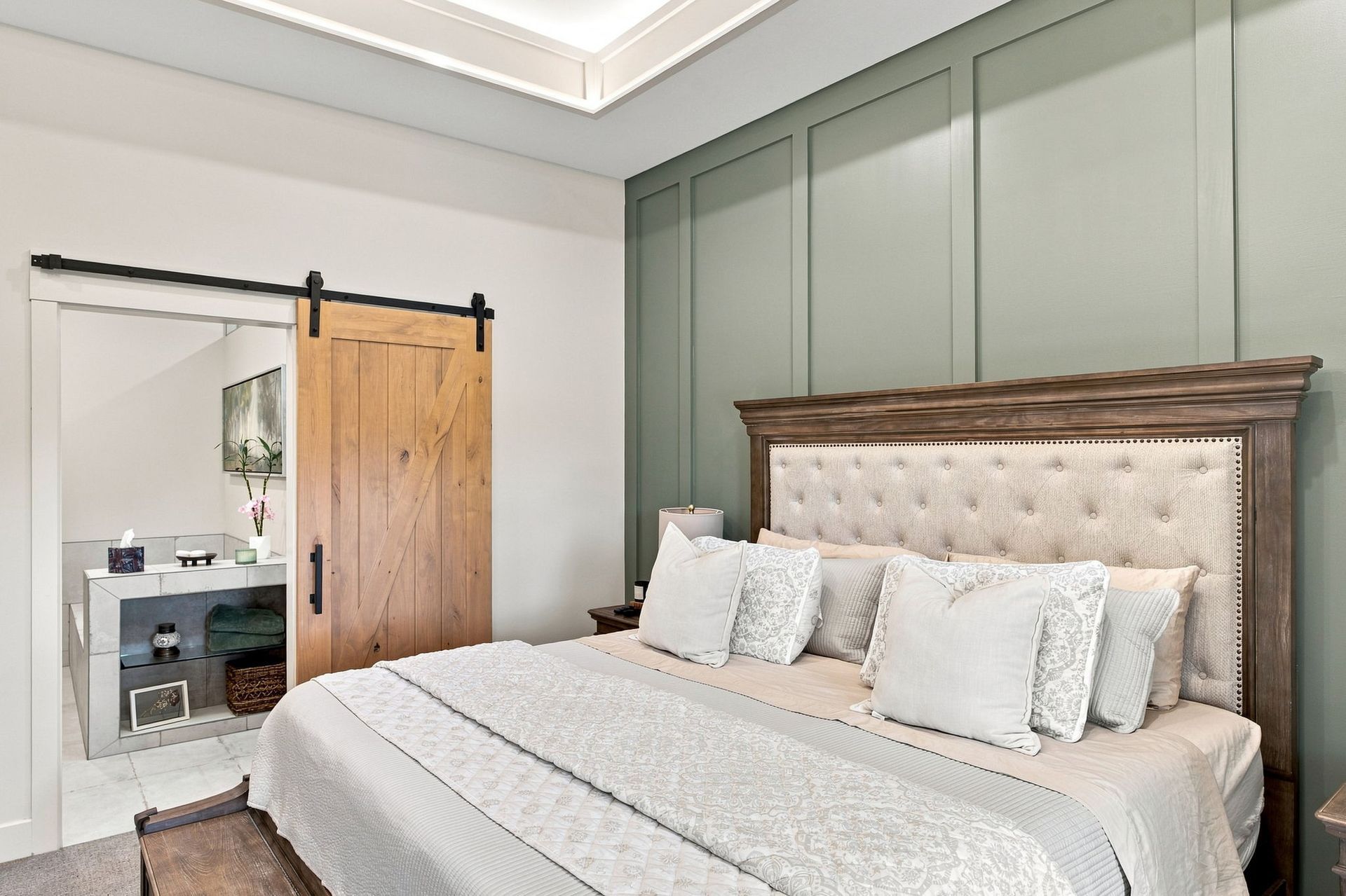 Bright bedroom with a large upholstered bed, green paneled wall, and rustic sliding barn door.