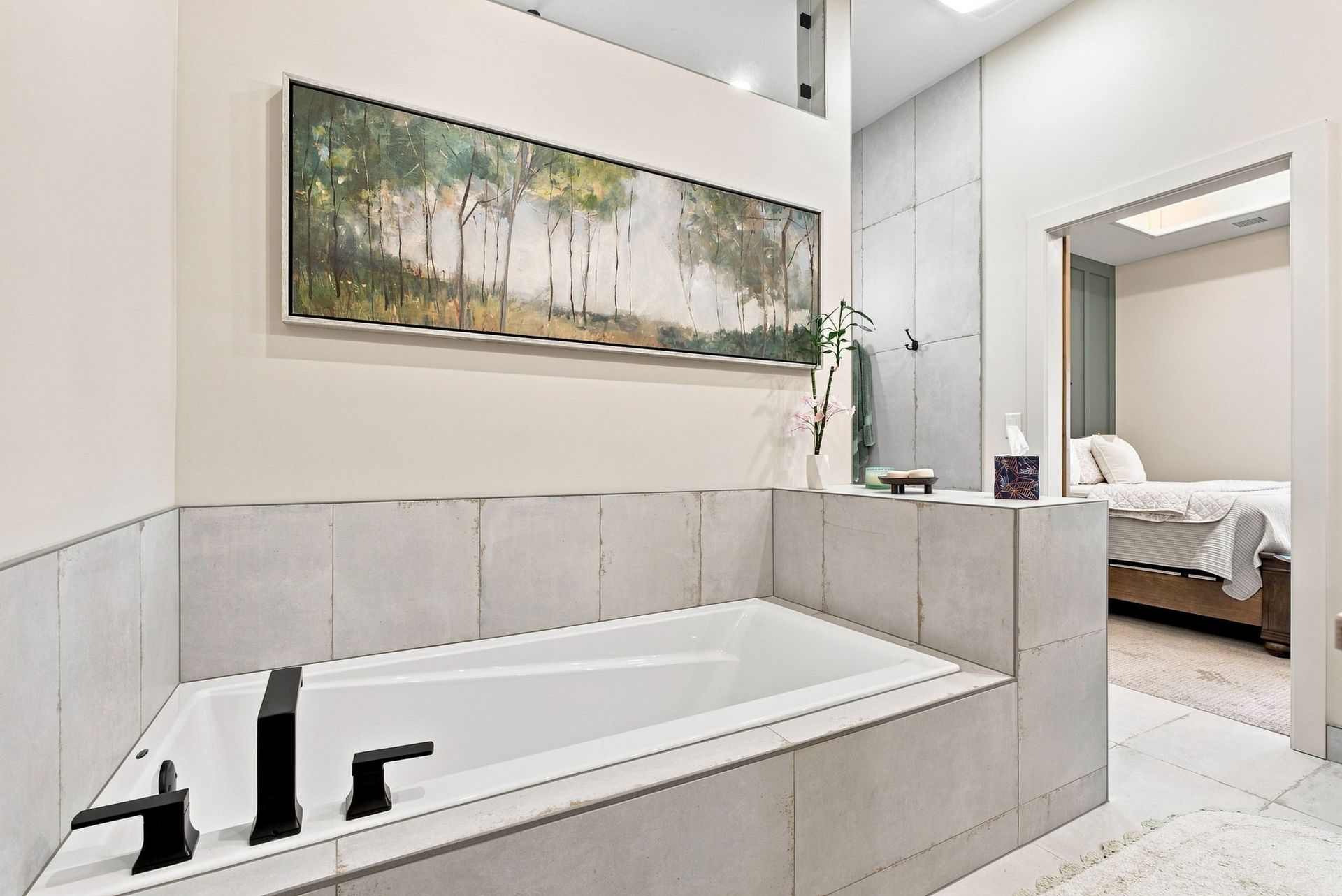 Modern bathroom with a white tub, beige tile, and framed landscape art above it
