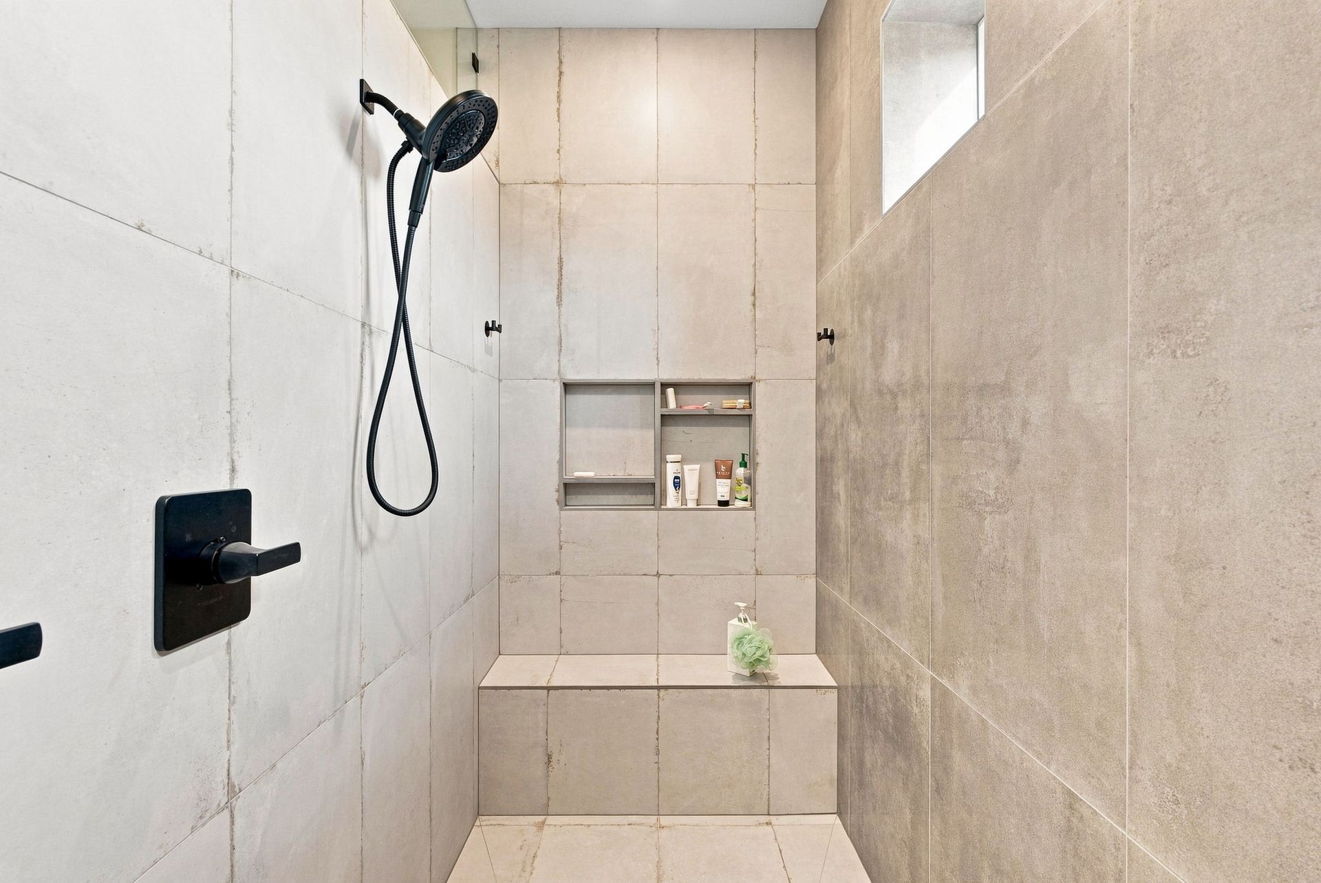 Modern bathroom shower with light tile, black showerhead, and built-in shelf.