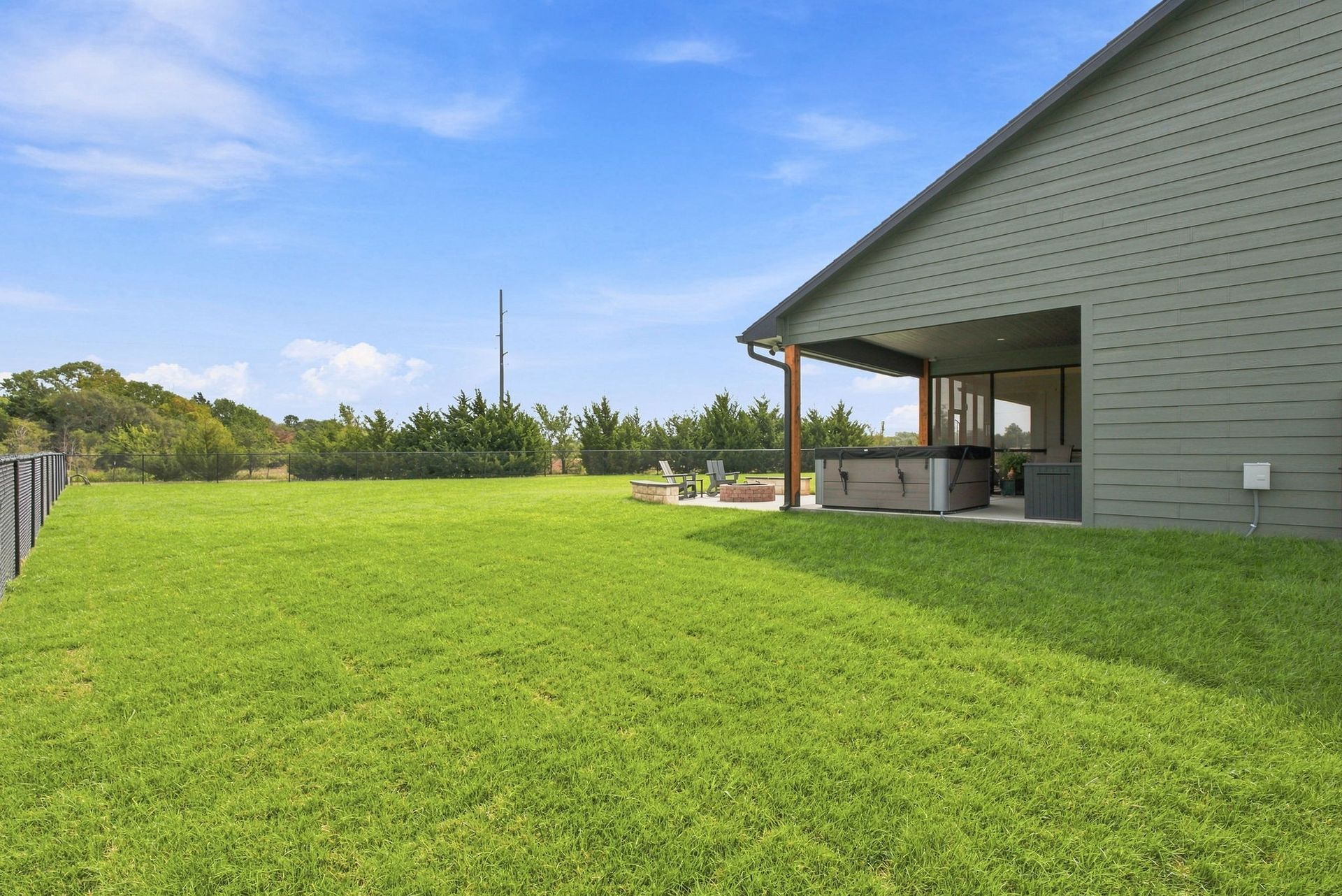 Green backyard beside a house with a covered patio and open lawn under a blue sky