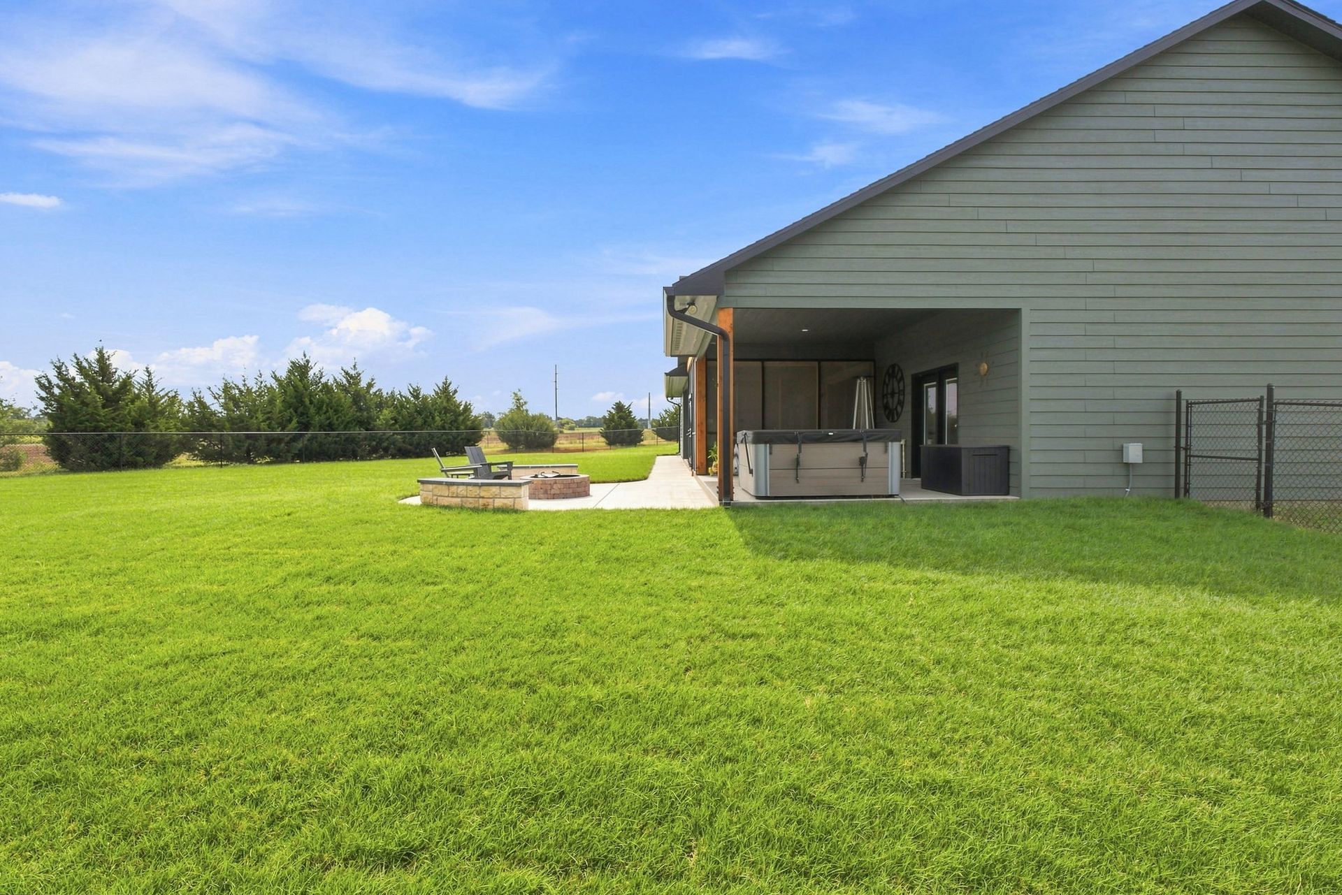 Backyard with lush green lawn, patio fire pit, and open-sided gray garage under a blue sky