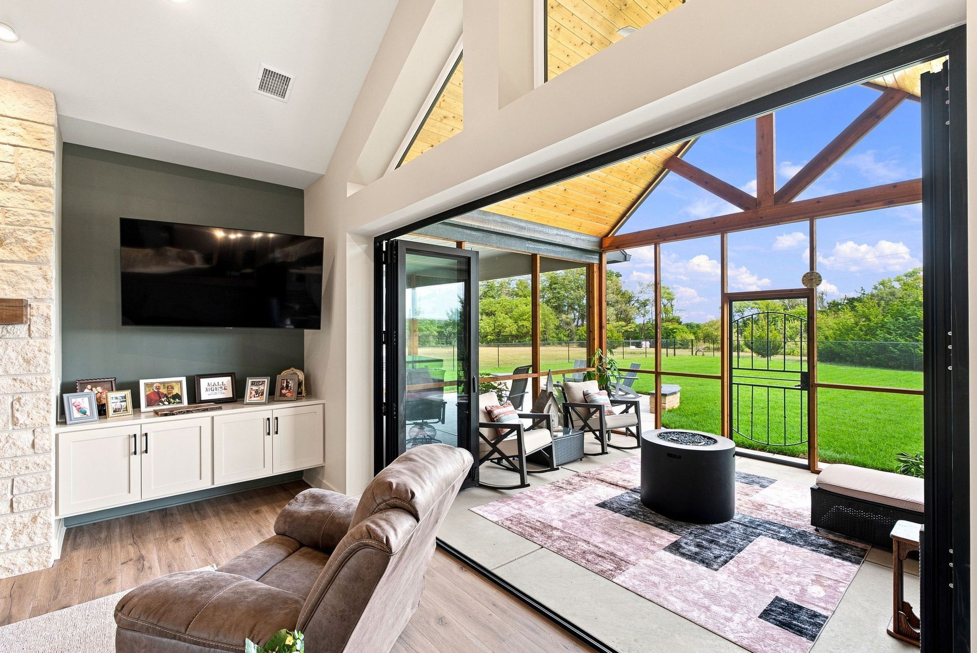 Modern living room with TV, leather sofa, and large glass doors opening to a covered patio and green yard