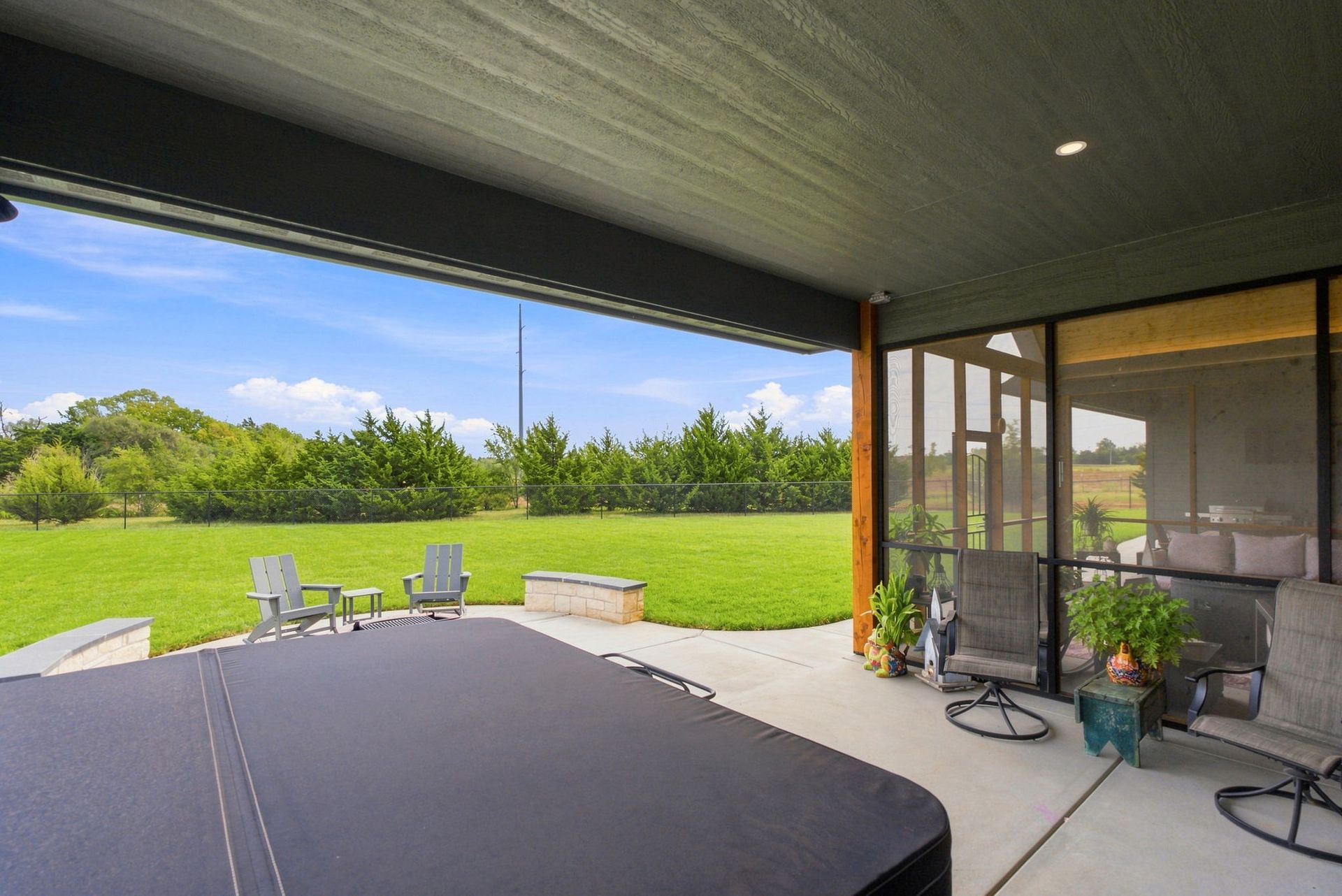 Covered patio with table, chairs, grill, and green lawn beyond a screened porch.