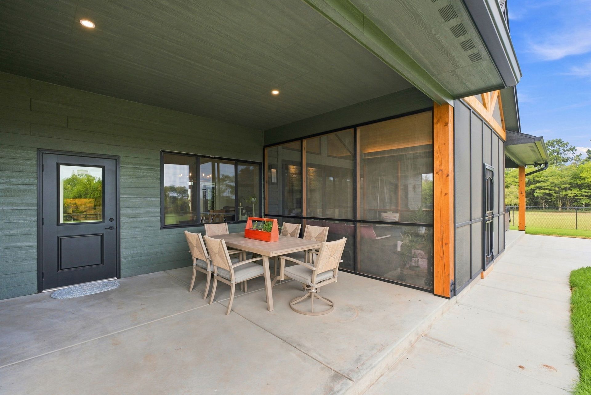 Covered patio with dining table and chairs beside a screened glass wall and dark door