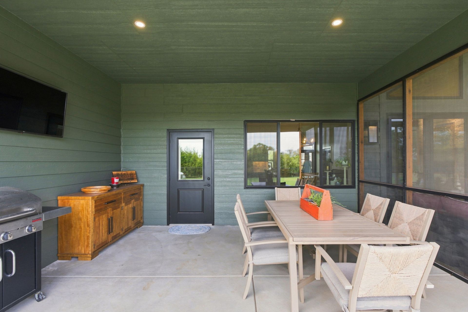 Covered patio with dining table, chairs, grill, and storage cabinet beside a screened window and door