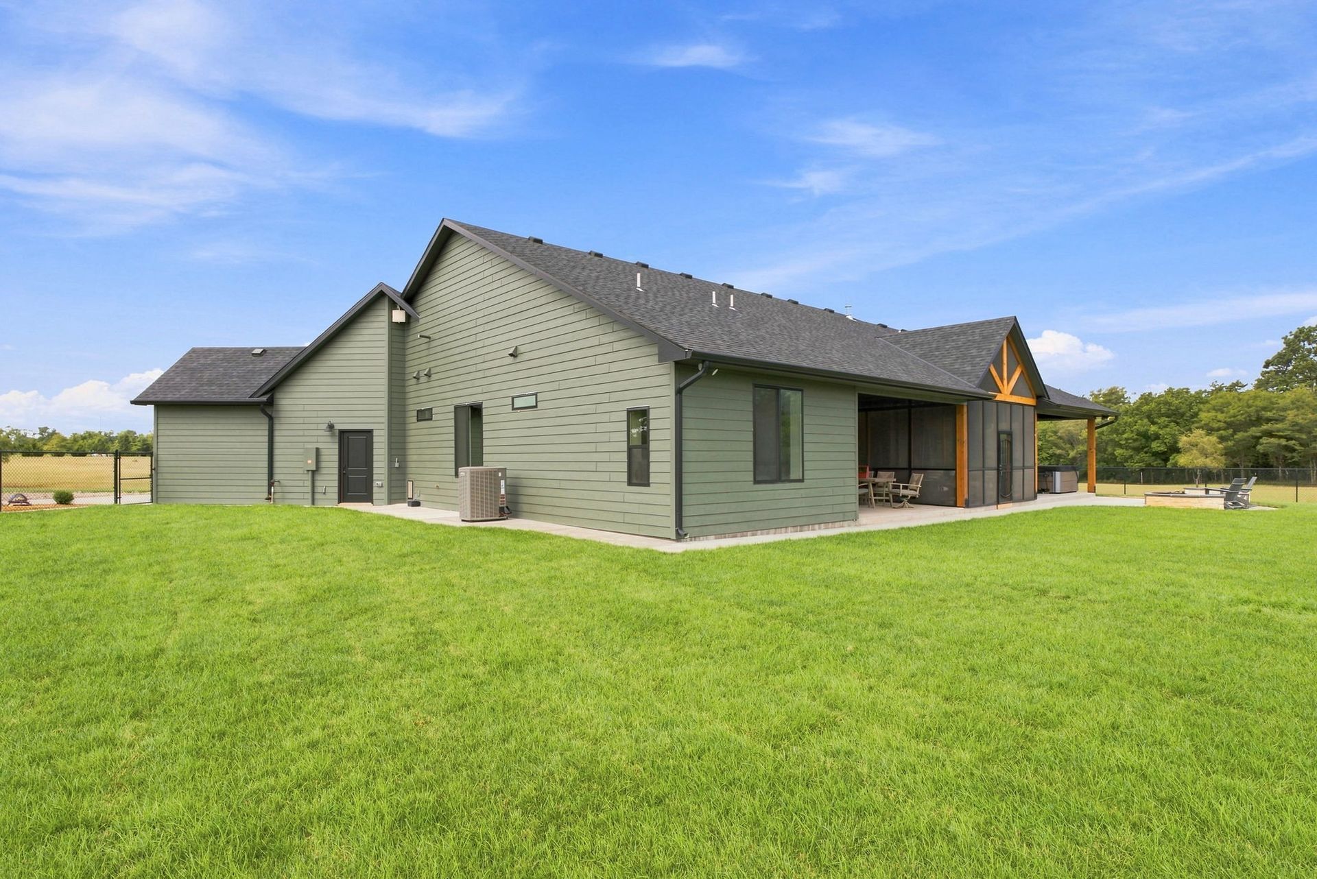 Single-story green house with a covered porch on a large grassy lawn under a blue sky
