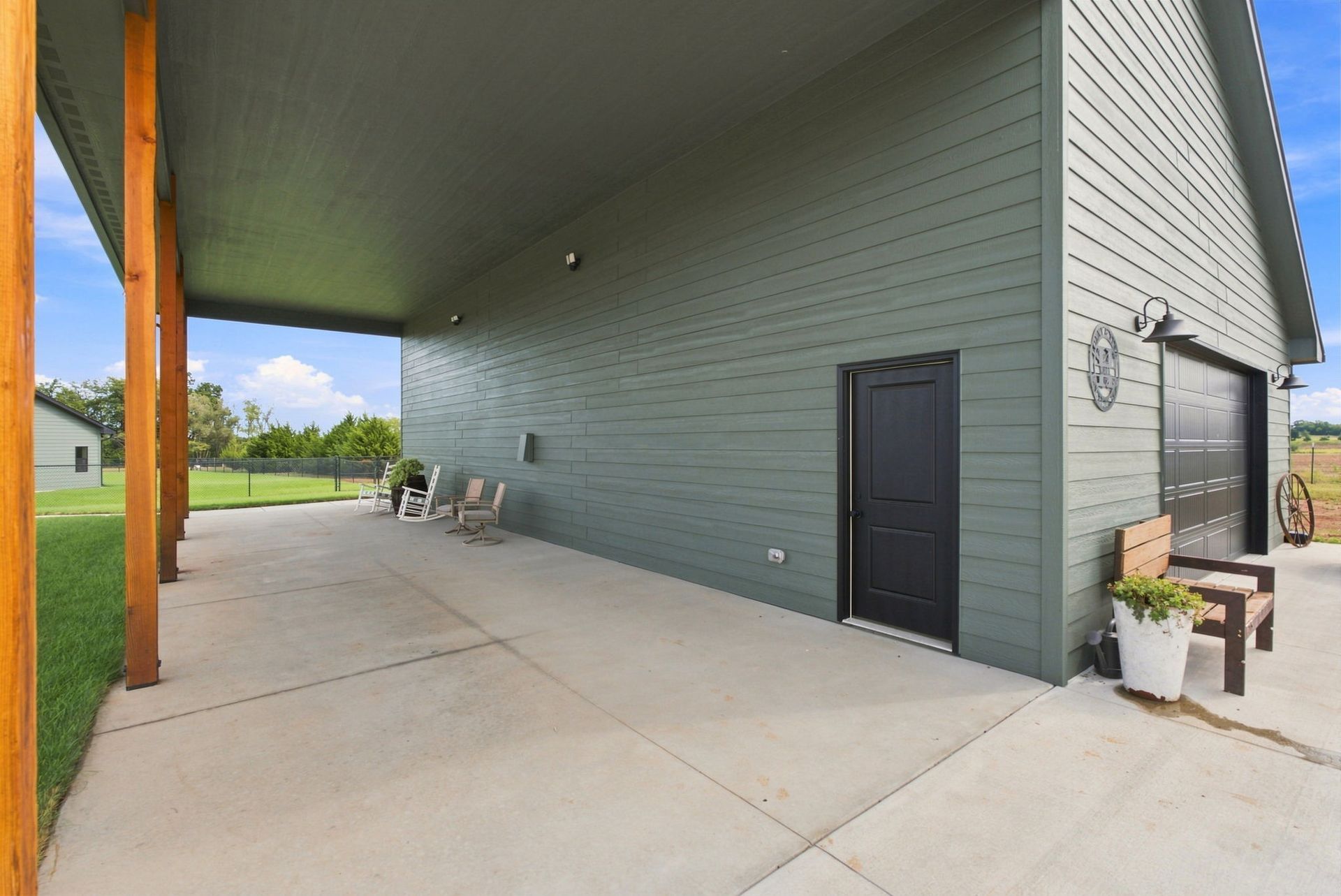 Covered concrete patio beside a gray building with a black door and outdoor seating
